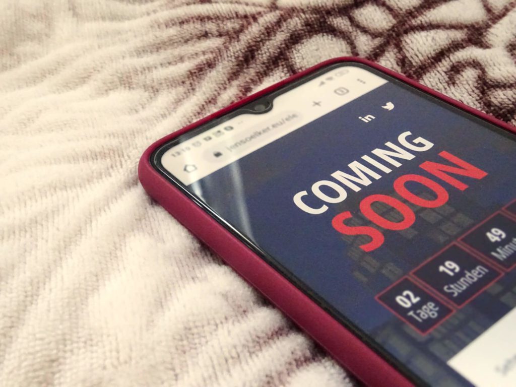 Auf dem Bild ist ein auf einer Decke liegendes Smartphone mit offener Website zu sehen, auf der "Coming Soon" steht.